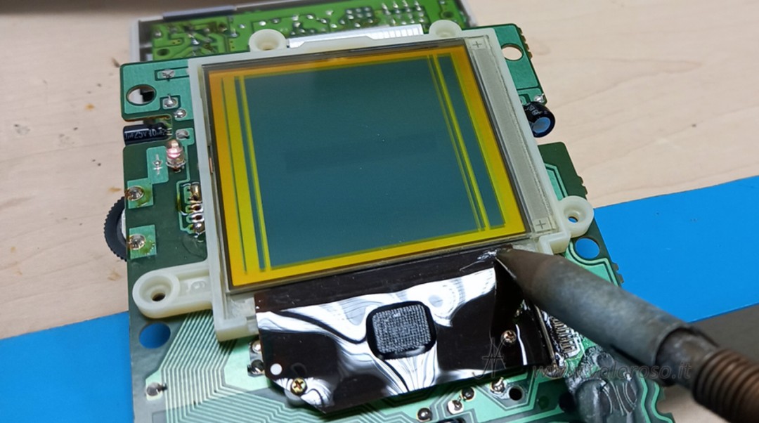 Application of controlled heat on the flat to reactivate the panel contacts. Crucial step in repairing Game Boy monitor vertical lines. Use of clean soldering iron without adding tin.